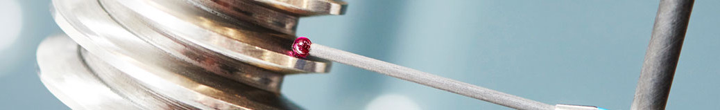 Close-up of a matchstick with a red tip held by a metallic clamp.
